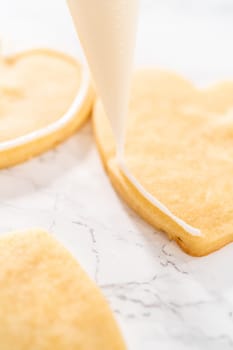 Decorating heart-shaped sugar cookies with pink and white royal icing for Valentine's Day.