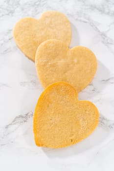 Decorating heart-shaped sugar cookies with pink and white royal icing for Valentine's Day.