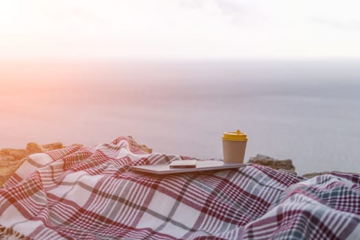 Laptop coffee on blanket with ocean view. Illustrating serene outdoor laptop use. Freelancer enjoying their time outdoors while working or browsing the internet