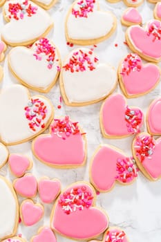 Decorating heart-shaped sugar cookies with pink and white royal icing for Valentine's Day.