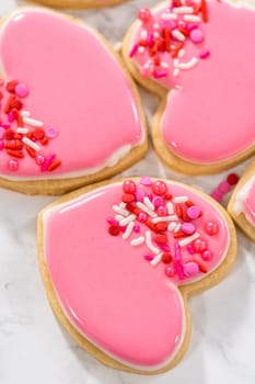 Decorating heart-shaped sugar cookies with pink and white royal icing for Valentine's Day.