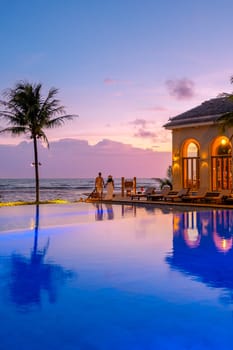 a young couple of men and women at a swimming pool during a vacation on a tropical island watching the sunset. man and woman at an infinity pool during sunset. luxury vacation in Thailand