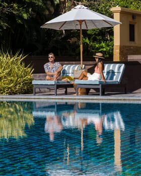 a young diverse couple of European men and Asian women at a swimming pool during a vacation on a tropical island watching the sunset. Infinity pool during sunset luxury vacation in Thailand