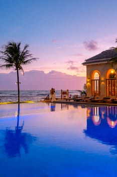 a young diverse couple of European men and Asian women at a swimming pool during a vacation on a tropical island watching the sunset. Infinity pool during sunset luxury vacation in Thailand