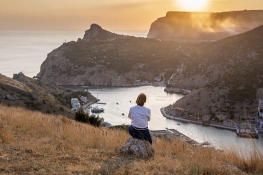 Happy woman on sunset in mountains. Woman siting with her back on the sunset in nature in summer. Silhouette