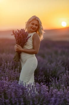 Blonde woman poses in lavender field at sunset. Happy woman in white dress holds lavender bouquet. Aromatherapy concept, lavender oil, photo session in lavender.