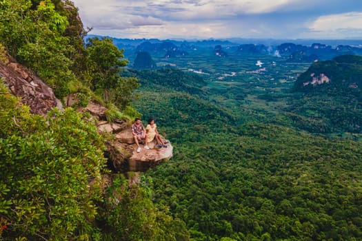 Dragon Crest Mountain Krabi Thailand, a Young couple sits on a rock that overhangs the abyss, with a beautiful landscape. Dragon Crest or Khuan Sai at Khao Ngon Nak Nature Trail in Krabi, Thailand