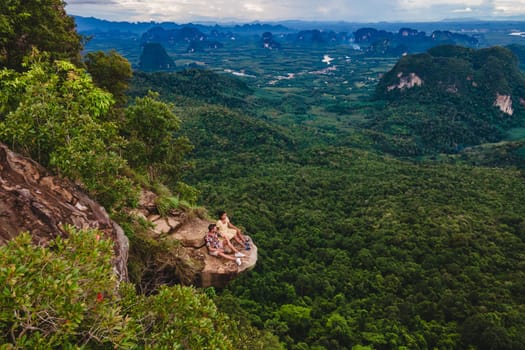 Dragon Crest Mountain Krabi Thailand, a Young couple sits on a rock that overhangs the abyss with a beautiful landscape. Dragon Crest or Khuan Sai at Khao Ngon Nak Nature Trail in Krabi rainforest