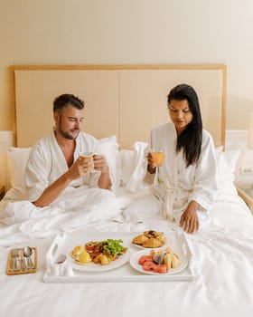 couple having breakfast in bed at a luxury hotel, men and women in bed with breakfast coffee, and bread. a diverse couple of an Asian woman and a European man in bedroom