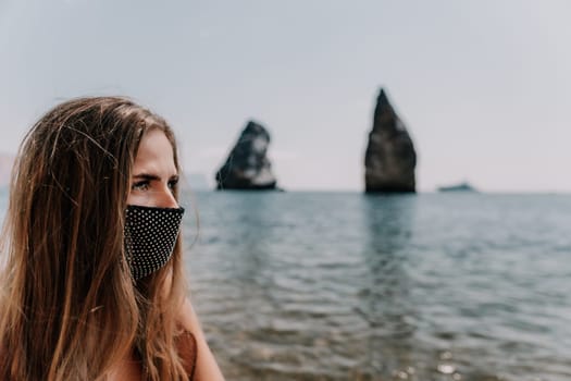 Woman travel sea. Young Happy woman in a long red dress posing on a beach near the sea on background of volcanic rocks, like in Iceland, sharing travel adventure journey