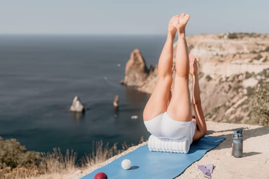 Middle aged well looking woman with black hair doing Pilates with the ring on the yoga mat near the sea on the pebble beach. Female fitness yoga concept. Healthy lifestyle, harmony and meditation.