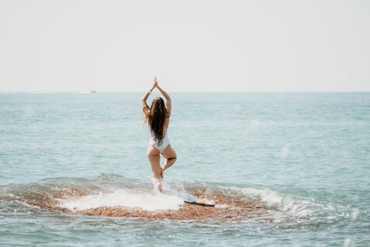 Woman sea yoga. Back view of free calm happy satisfied woman with long hair standing on top rock with yoga position against of sky by the sea. Healthy lifestyle outdoors in nature, fitness concept.