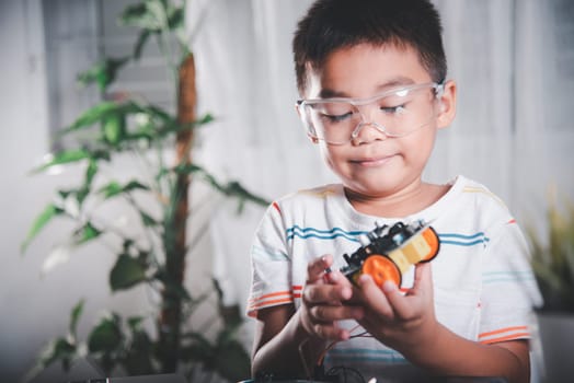 Little child trying assemble build wheel to car toy, Asian kid boy assembling wheel into Arduino robot car homework, creating electronic AI technology workshop online school lesson