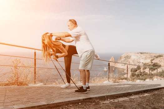 Happy Middle aged couple or friends practicing nordic walking in park near sea. Mature couple with trekking poles walking, practicing Nordic walking outdoors. Aging youthfully and sport concept.