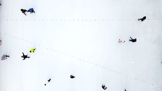 Many people skating on white ice skating rink outdoors on winter day top view. Aerial drone view. New Year Christmas celebration holidays recreation sport enjoying lifestyle sportive fun background.