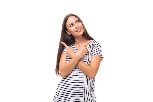 young pretty caucasian brunette woman in a striped t-shirt points her hand to the side on a white background with copy space.