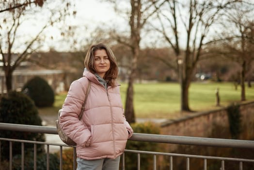 Young beautiful pretty tourist girl in warm hat and coat with backpack walking at cold autumn in Europe city enjoying her travel in Zurich Switzerland. Outdoor portrait of young tourist woman enjoying sightseeing