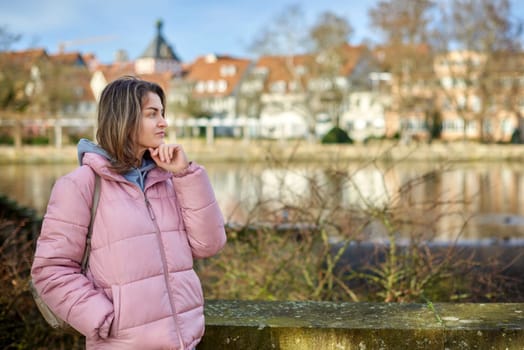 Young beautiful pretty tourist girl in warm hat and coat with backpack walking at cold autumn in Europe city enjoying her travel in Zurich Switzerland. Outdoor portrait of young tourist woman enjoying sightseeing