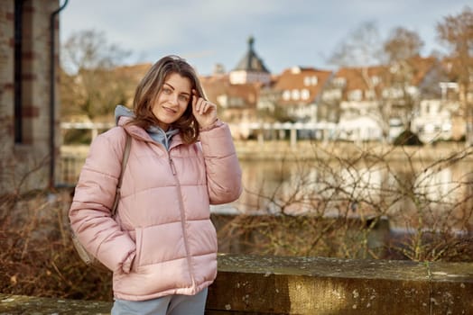 Young beautiful pretty tourist girl in warm hat and coat with backpack walking at cold autumn in Europe city enjoying her travel in Zurich Switzerland. Outdoor portrait of young tourist woman enjoying sightseeing