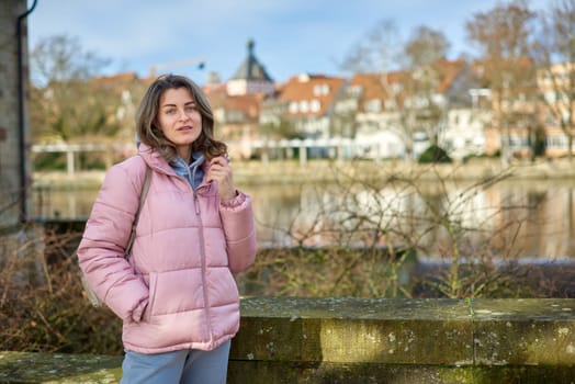 Young beautiful pretty tourist girl in warm hat and coat with backpack walking at cold autumn in Europe city enjoying her travel in Zurich Switzerland. Outdoor portrait of young tourist woman enjoying sightseeing