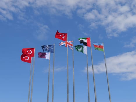 The photograph showcases a collection of national flags including those of Turkey, Qatar, the UK, the UAE, Pakistan, and Azerbaijan, as well as the NATO flag, all standing tall against a cloudless sky.