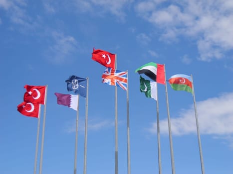 A vibrant display of national flags, including Turkey, the United Kingdom, the United Arab Emirates, and Azerbaijan, alongside the flag of NATO, fluttering proudly against a clear blue sky