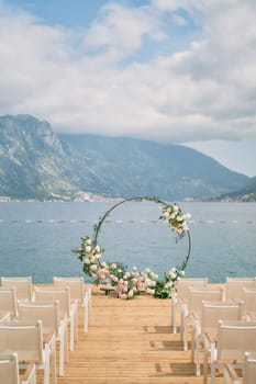 Round wedding arch stands on the pier in front of the chairs. High quality photo