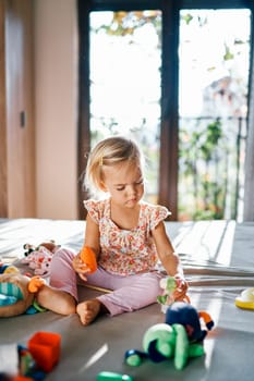 Little girl plays with a plush dinosaur on the bed among soft toys. High quality photo