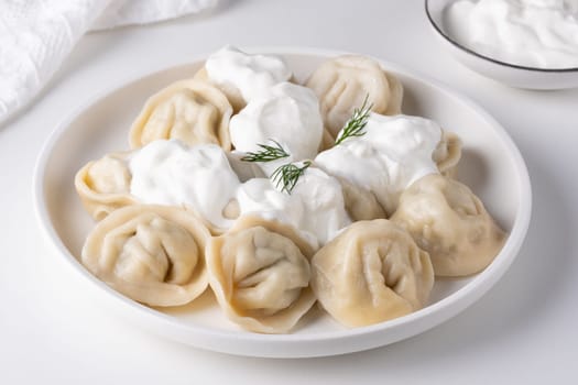 Traditional russian pelmeni, ravioli, dumplings with meat and sour cream in a white plate.
