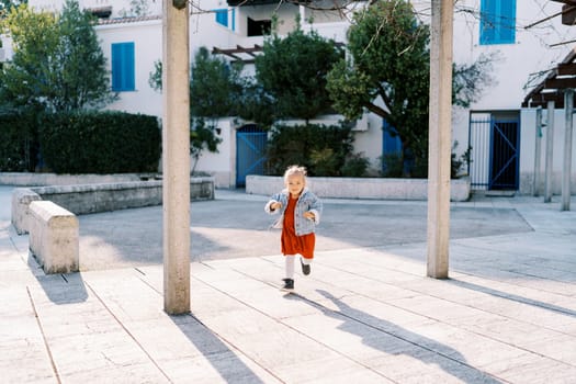 Little girl runs through the tiled courtyard near the three-story house between the columns. High quality photo