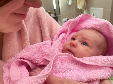 Woman Holding a newborn Baby after bathing in a Pink Towel. Close up cute newborn baby wrapped in bath towel