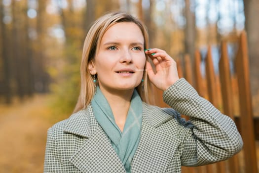 Blonde woman in elegant gray coat walks in the sunny autumn season park. Generation z and gen z youth concept