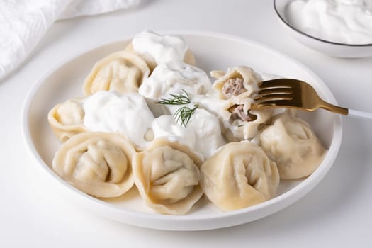 Traditional russian pelmeni, ravioli, dumplings with meat and sour cream in a white plate.