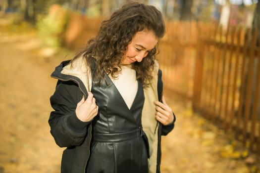 Attractive young woman walking in autumn park, happy mood and fashion style trend and curly long brown hair. Fall season and pretty female portrait. Millennial generation