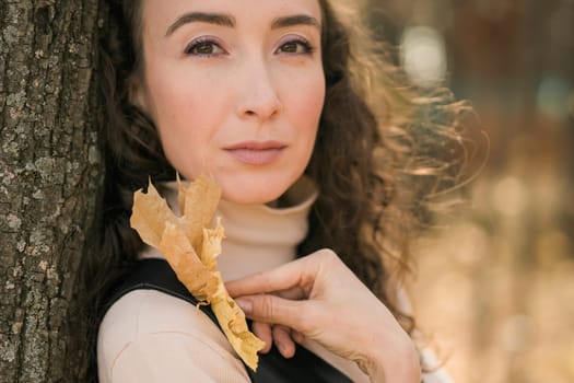 Attractive young woman walking in autumn park, happy mood and fashion style trend and curly long brown hair. Fall season and pretty female portrait. Millennial generation