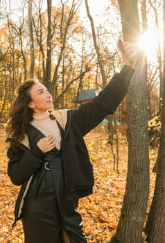 Attractive young woman walking in autumn park, happy mood and fashion style trend and curly long brown hair. Fall season and pretty female portrait. Millennial generation