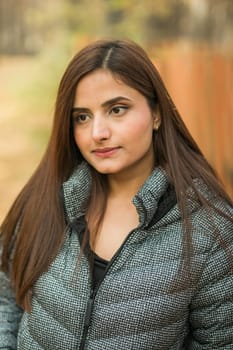 Close-up portrait of a young beautiful confident Indian Asian woman in fall outdoor. Happy and natural smiling female. Generation z and gen z youth