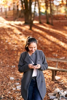 Smiling girl looks into a mug with tea in her hands in an autumn park. High quality photo