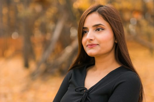 Close-up portrait of a young beautiful confident Indian Asian woman in fall outdoor. Happy and natural smiling female. Generation z and gen z youth