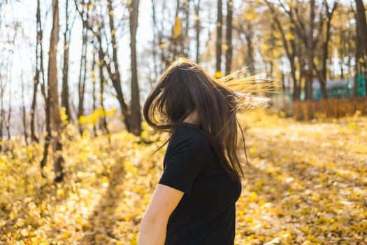 Cute young woman with long fluffy hair dancing in a park at sunset. Beautiful young woman with brown hair dance in a forest at sunset. Freedom and season nature concept. Soft focus.