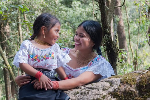 complicit glances between a young mother and her young daughter native ecuadorian women in the jungle of ecuador with traditional dresses of their culture of cotacachi. women's day. High quality photo