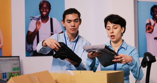 Diverse store managers preparing packages for shipping, putting stylish clothes in carton boxes in modern boutique. Employees working at clients orders, discussing delivery details in shopping mall