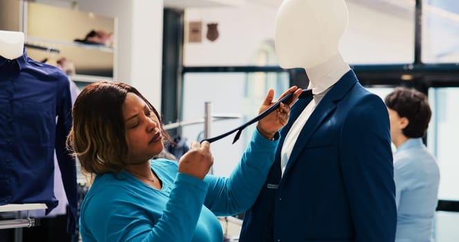 African american shopper analyzing at blue suit, checking merchandise material in clothing store. Shopaholic customer shopping for fashionable clothes, looking at new fashion collection