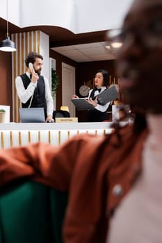 Hotel staff working on reservations at front desk with records, using landline phone to make online bookings at reception counter in lobby. Man and woman receptionists doing check in.