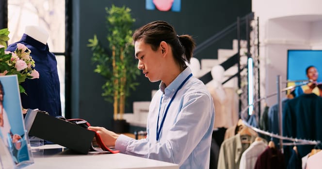 Asian manager arranging stylish accessories, working at modern boutique visual. Employee checking hangers and racks full with fashionable merchandise in clothing store. Fashion concept