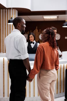 African american guests in lobby, holding hands at front desk to fill in registration files. Young people feeling joyful upon their arrival at luxury hotel for room booking, reception.