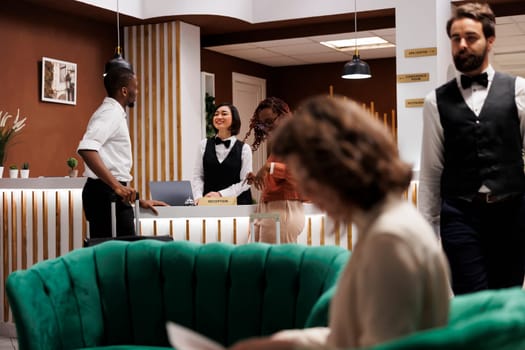 Man welcoming people at front desk, providing excellent service with registration at hotel. Male reception worker talking to guests in lobby, looking to book room at resort upon their arrival.