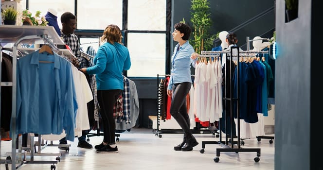 Fashionable couple shopping for elegant shirt, analyzing clothes material before buying it in modern boutique. Stylish customers looking at hangers with new fashion collection in clothing store