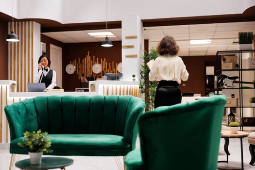 Hotel concierge checking record forms in lounge area at reception, reviewing registration files and booking bureaucracy. Female manager working on providing excellent service for guests.