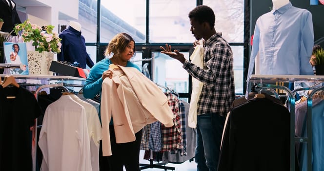 African american couple checking stylish merchandise, shopping for casual wear in modern boutique. Fashionable customers analyzing trendy outfit material in clothing store. Fashion concept